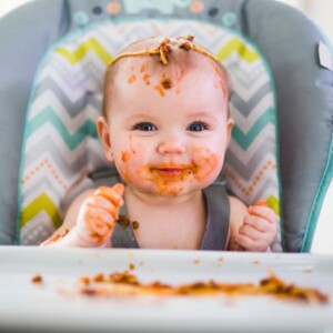 zadowolony ubrudzony jedzeniem niemowlak siedzący w krzesełku do karmienia